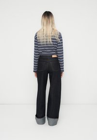 Bredde ben mørke denim jeans med en brettet lys blå mansjett, kombinert med en marineblå og hvit stripete langermet topp. Bakvisning.