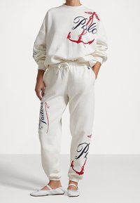 Vitt bomullssvettshirt- och byxset med röda och blå ankare samt textdesign. Avslappnad passform med elastisk dragsko i midjan.