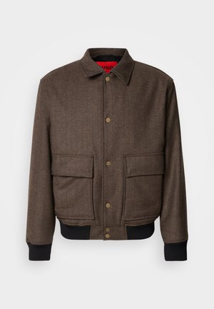 Brown herringbone jacket with a button closure, two front pockets, and ribbed cuffs. Lined with red fabric for added detail.