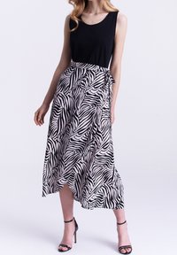 Zwarte mouwloze top gecombineerd met een maxi rok met zebraprint, voorzien van een vloeiende uitstraling en een strik in de taille. Zwarte hoge hakken sandalen.