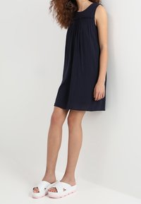 Vestido sin mangas azul marino con pliegues en el pecho, hecho de tela ligera. Combinado con sandalias blancas con suela gruesa de color rosa.