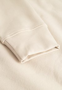 Beige sweatshirt fabric with a folded cuff, featuring a smooth texture and subtle stitching detail. Simple, functional design.