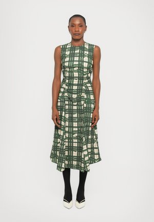 Green and cream plaid dress with a fitted bodice, gathered details, and a flared hem. Paired with black tights and two-tone heels.