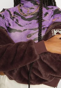 Fioletowy sweter z golfem w czarne tygrysie paski, zestawiony z brązową, futrzaną, oversize'ową kurtką z prążkowanymi mankietami i detalem z logo.