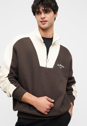 Brun og cremefarvet sweatshirt med halv lynlås, V-formet design, ribstrikkede manchetter og broderet logodetalje på brystet. Blød bomuldsblanding.