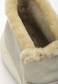 Grijze suede sneaker met een beige nepbonten voering rond de enkel, die een gladde textuur en een ronde vorm laat zien. Witte rubberen zool zichtbaar.