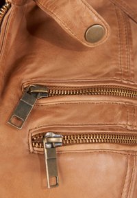 Bruine leren tas met twee ritsen aan de voorkant met metalen trekstangen. De gladde textuur en subtiele nerfpatroon accentueren het ontwerp.