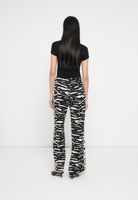 Haut noir ajusté associé à un pantalon à jambes larges présentant un imprimé zèbre beige et noir. Tissu lisse avec une silhouette décontractée, porté avec des talons.
