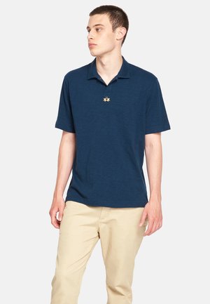Marineblå polo shirt lavet af struktureret stof, med en tre-knaps lukning og et lille broderet design på brystet.