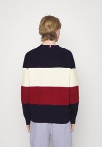 Maglione a righe navy blu, crema e rosso con un design a maglia testurizzata. Colletto e polsini a coste; dettaglio verticale sul retro.