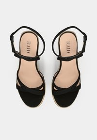 Black espadrille sandals with crisscross straps, open toe design, and a textured, natural woven sole. The insole features a subtle logo.