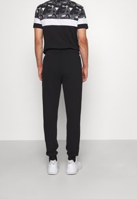 Pantaloni jogger neri con finitura testurizzata, vita elasticizzata e orli a costine; abbinati a una maglietta a maniche corte con grafica bianca e nera.