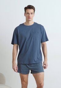 Marineblauwe katoenen T-shirt met korte mouwen en een borstzak, gecombineerd met bijpassende shorts, beide met een gladde textuur.