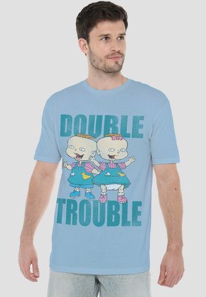 Light blue T-shirt featuring a graphic print of cartoon characters in overalls, with "DOUBLE TROUBLE" text in bold teal. Short sleeves.