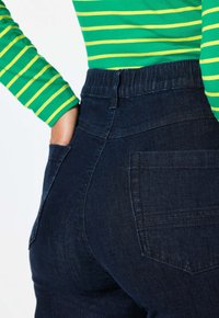 Jeans de mezclilla azul oscuro con una cintura alta y bolsillos traseros, combinados con una camisa de manga larga a rayas verdes y amarillas.