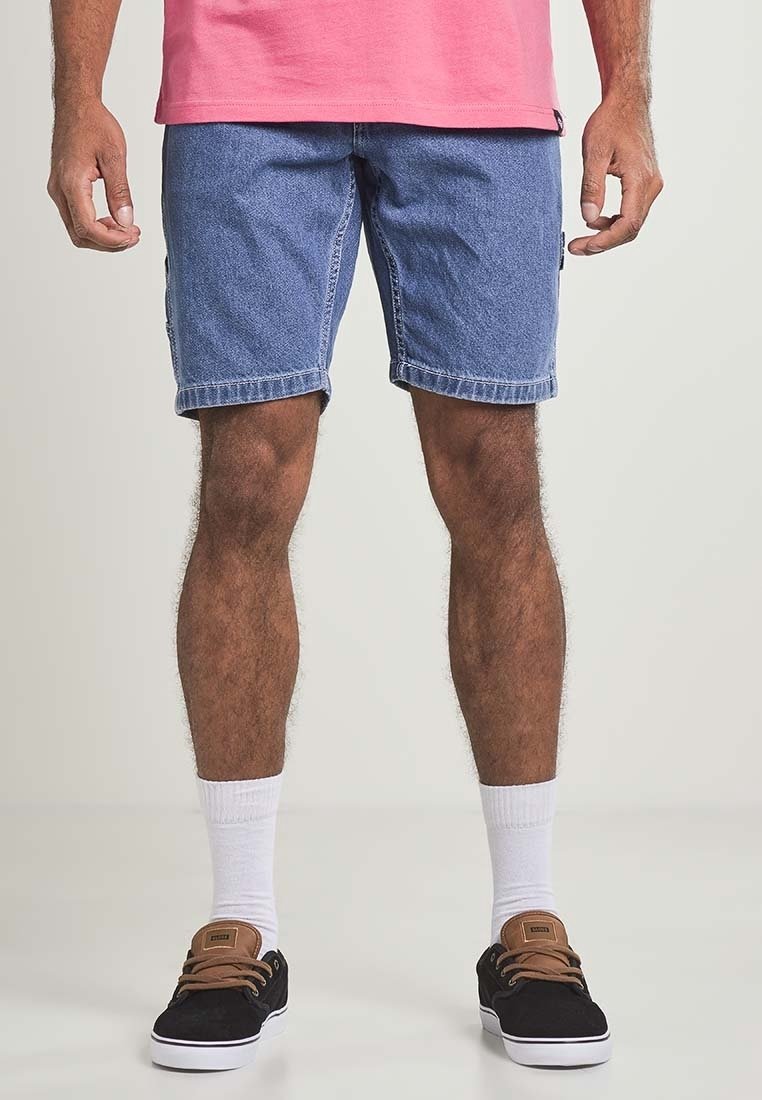 Shorts en denim bleu clair avec une coupe décontractée, ourlets retroussés, deux poches latérales, portés avec des chaussures noires et des chaussettes blanches montantes.