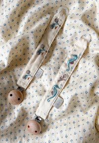 Cloth pacifier clips with beige fabric, featuring embroidered designs of bicycles and seahorses, wooden beads, and metal clips.