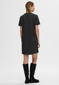 Robe t-shirt noire courte avec des manches courtes, coupe droite et col rond, associée à des bottes en cuir noir hautes jusqu'aux genoux.