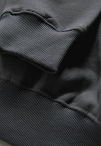 Donkergrijze sweatshirt van dichtbij, met ribbelachtige textuur, gladde stof en gestikte naden bij de mouwen en de zoom.
