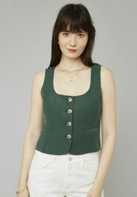 Haut court sans manches vert avec un décolleté carré, des boutons sur le devant et de petites poches latérales, fabriqué à partir d'un tissu texturé.