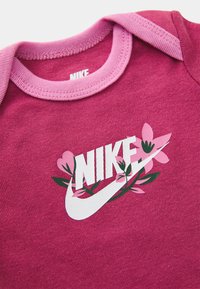 T-shirt de algodão roxa com um colarinho canelado rosa e um logótipo Nike impresso em branco rodeado por desenhos florais em rosa e verde.