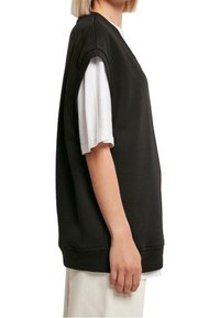 Czarna, oversize'owa bluza z krótkimi rękawami, noszona na białej koszulce. Charakteryzuje się luźnym krojem i prostym, nowoczesnym wzornictwem.