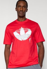 Κόκκινο βαμβακερό μπλουζάκι με γραφικό σχέδιο από ένα λευκό έμβλημα με το κείμενο «You'll Never Walk Alone» και το λογότυπο της Liverpool F.C.