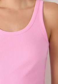 Prążkowany top w jasnoróżowym kolorze z okrągłym dekoltem. Posiada cienkie ramiączka oraz dopasowany krój, podkreślający gładką, elastyczną teksturę.