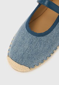 Espadrilă din denim cu vârf rotund, partea superioară bleumarin și talpă exterioară din iută țesută. Prezintă o cusătură decorativă de-a lungul marginii.