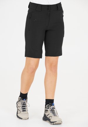 Black shorts with a fitted design, made from stretch fabric. Features zippered pockets and a flat waistband. Worn with beige hiking shoes.