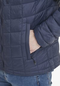 Mörkblå vadderad jacka med quiltat mönster, med en sidoficka och dragkedja, tillverkad av lätt, strukturerad tyg.