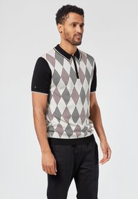 Lyhythihainen polo-paita mustalla kauluksella, jossa on teksturoitu timanttikuvio vaaleassa beigeessä, viininpunaisessa ja mustassa. Ribbaus helman ja hihansuiden ympärillä.