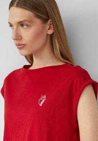 Rode katoenen t-shirt met opgerolde mouwen en een klein wit grafisch ontwerp op de borst. Zachte textuur, casual pasvorm.