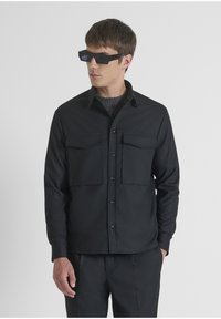 Zwarte lange mouwen shirt met een knoopsluiting aan de voorkant, twee borstzakken en een rechte zoom. Gladde stof met een gestructureerde kraag en manchetten.