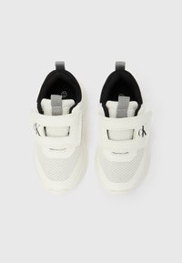 Ténis brancos com parte superior em malha, forro preto e detalhes cinzentos. Apresentam tira de velcro ajustável e uma alça para puxar no calcanhar.