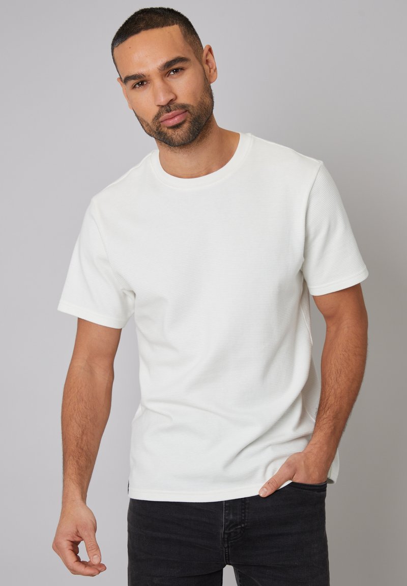 Hvid kortærmet t-shirt med rund hals, ribbet tekstur og en afslappet pasform, parret med mørk denim jeans.