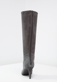 Botte en daim gris montante avec un talon aiguille et une fermeture éclair à l'arrière, présentant une texture lisse et une section inférieure contrastante.