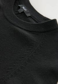 Pull noir avec un col rond, des poignets côtelés et un ourlet côtelé. Texture douce avec des détails subtils le long des coutures. Étiquette indiquant "NEXT."