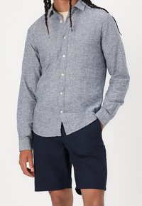 Lichtblauw linnen overhemd met knopen, lange mouwen, een klassieke kraag en een ronde zoom, gecombineerd met marineblauwe shorts.