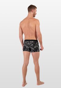 Černé boxerky s květinovým vzorem, s elastickým pasem a přiléhavým střihem, vystavené na nahém mužském modelu.