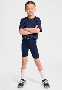 Navyblå sportoutfit bestående av en kortärmad tröja och tajta shorts. Inkluderar en märkt midjeband och sportiga sneakers med vita strumpor.