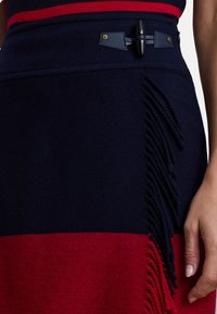 Pletená sukňa s dizajnom v námorníckej a červenej farbe, textúrovaná so strapcami na bokoch a dekoratívnym zapínaním na gombík v páse.