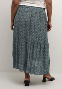 Maxi spódnica w zielono-niebieski wzór paisley, z marszczonym pasem i lejącym się materiałem, noszona z czarnymi mule na wysokim obcasie.