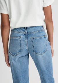 Lichtblauwe denim jeans met een hoge taille, rechte pijpen, kenmerkende achterzakken en zichtbare stikseldetails.