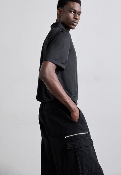 Svart kortermet polo skjorte med teksturert overflate, sammen med svarte cargo shorts med glidelås- og lommeposer.