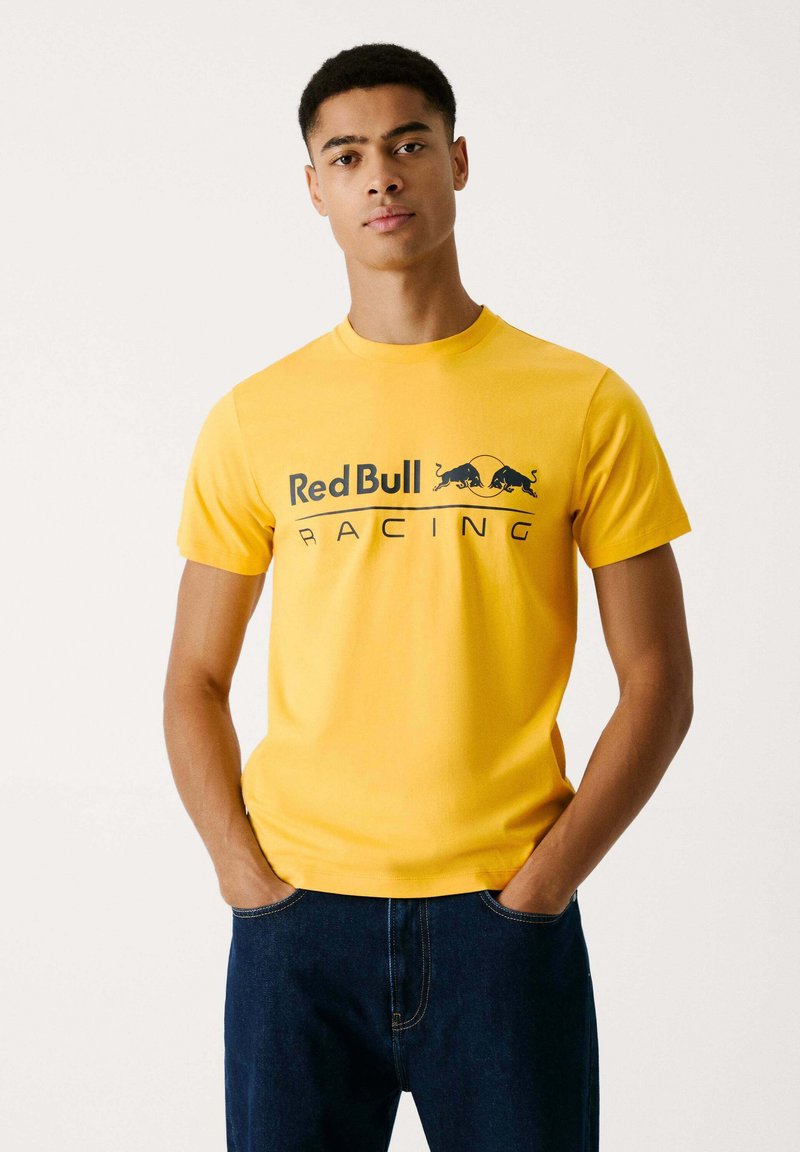 Dzeltena kokvilnas T-krekls ar īsām piedurknēm. Ar melnu "Red Bull Racing" grafiku uz krūtīm. Viens tonis, ikdienas piegriezums.