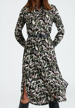 Robe longue à boutons avec un imprimé abstrait vert, noir et blanc. Comprend des manches longues, une taille ceinturée et des fentes latérales. Fabriquée en tissu léger.