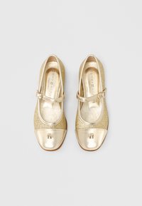 Χρυσά παπούτσια Mary Jane με μεταλλική στρογγυλή μύτη, λαμπερό τακούνι και ρυθμιζόμενο λουράκι. Διαθέτουν λογότυπο διακοσμητικό στη μύτη.