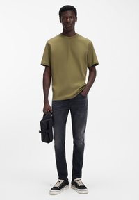 Oliivinvihreä puuvillainen t-paita, rento malli, pyöreä pääntie, yhdistetty tummanharmaisiin slim fit -farkkuihin, musta laukku kädessä, päällä mustavalkoiset tennarit.