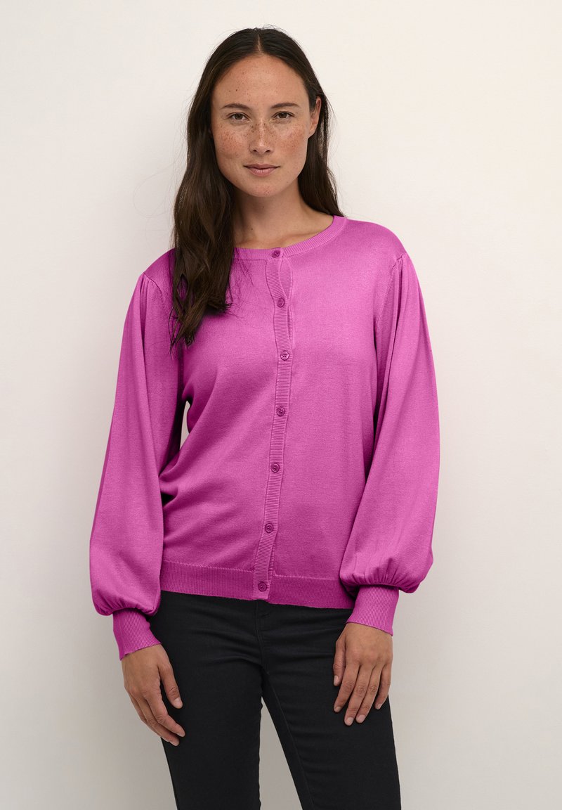 Rosa Strickjacke mit langen Puffärmeln, gerippten Bündchen und Knopfverschluss. Der Stoff wirkt glatt und leicht, ideal zum Drunterziehen.